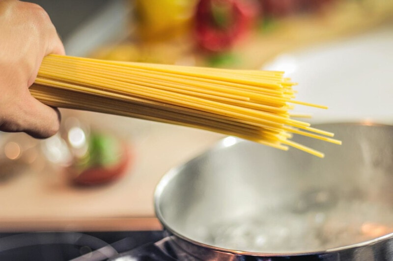 Hand holding uncooked spaghetti over a pot of boiling water.