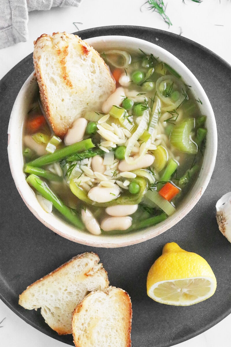 Spring minestrone soup with bread in a white bowl.