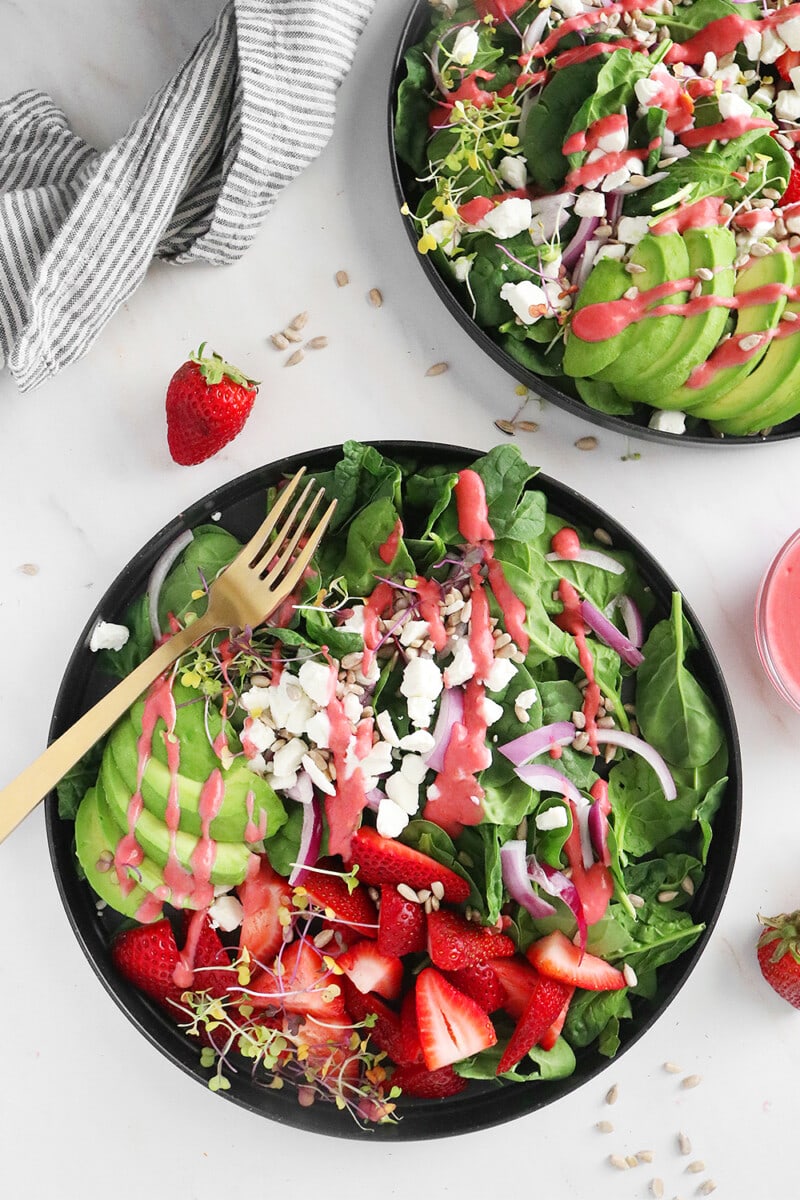 Spinach salad topped with stawberries, avocado, goat cheese, and raspberry vinaigrette in a bowl.