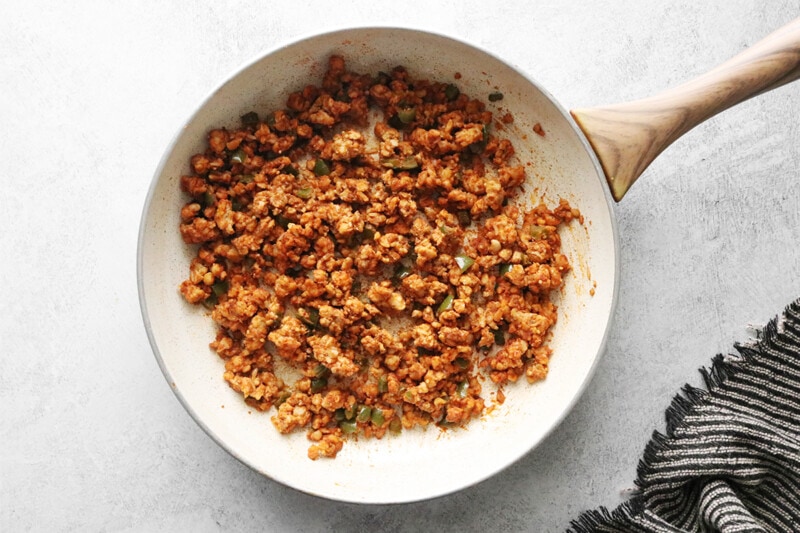 Adding taco seasoning and broth to tempeh in a skillet