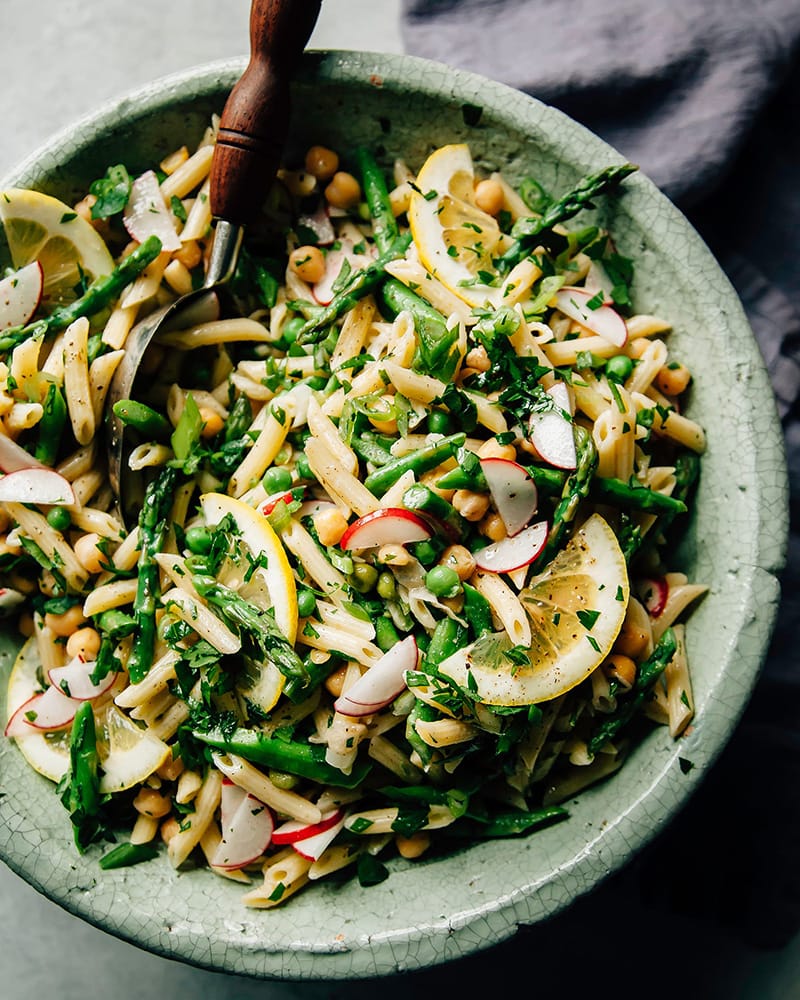 Fresh pasta salad with asparagus, chickpeas, green peas, and radishes in a bowl.