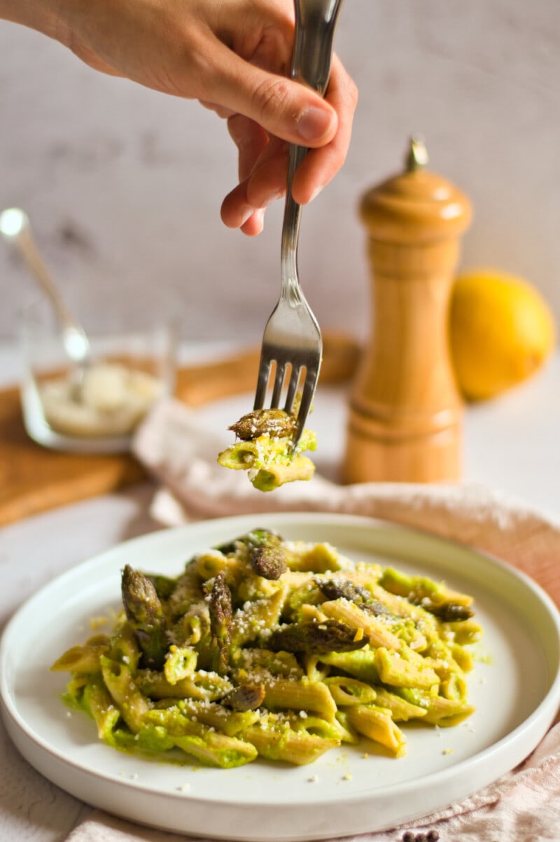 Vegan Asparagus Pasta on a plate with a hand holding a fork.