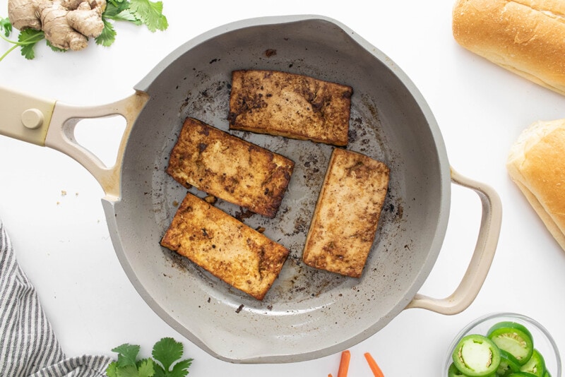 Cooking tofu for vegan bánh mì in a skillet until crispy.