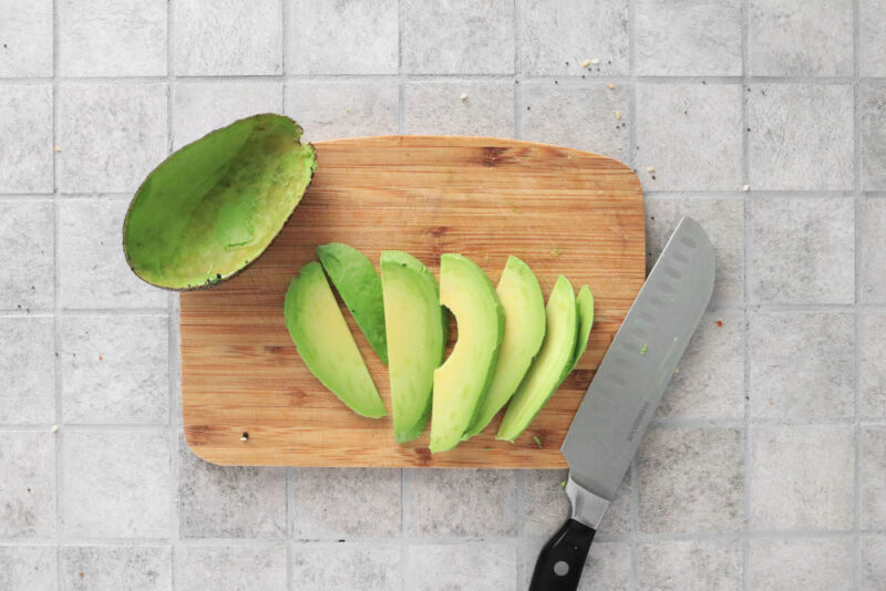 Sliced avocado on a cutting board with a knife.