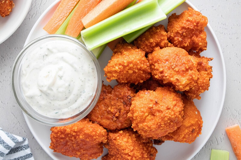 A plate of crispy vegan buffalo cauliflower wings served with a bowl of vegan ranch and celery and carrot sticks.