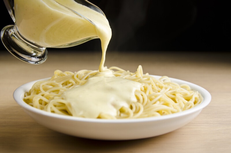Creamy vegan cheese sauce pouring over pasta