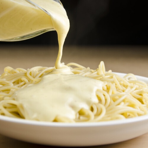 Creamy vegan cheese sauce pouring over pasta