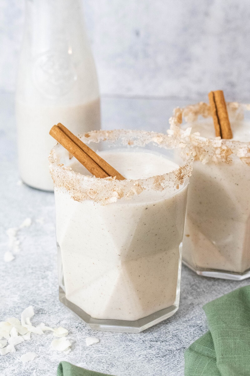Vegan coquito in a glass, garnished with cinnamon sticks.