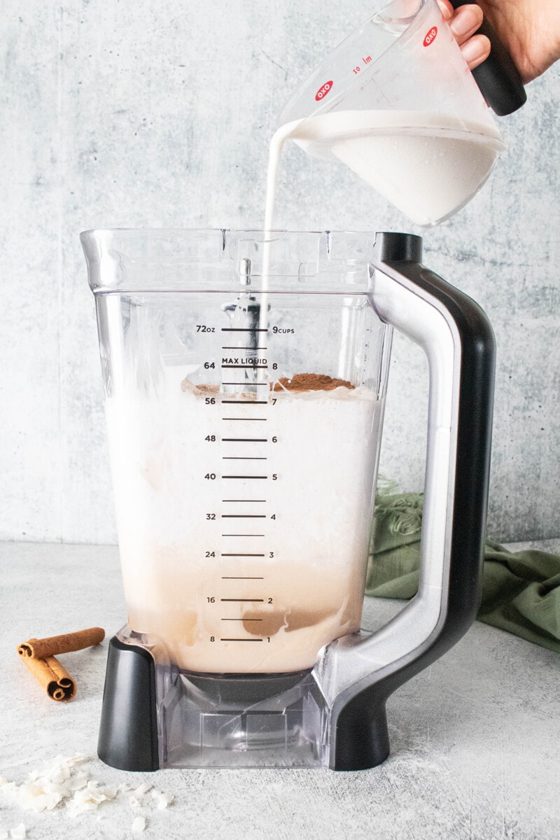 Pouring liquid vegan coquito ingredients into a blender.
