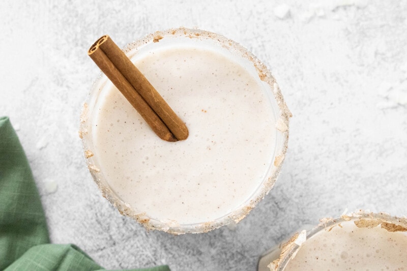 Vegan coquito in a glass with a cinnamon stick.