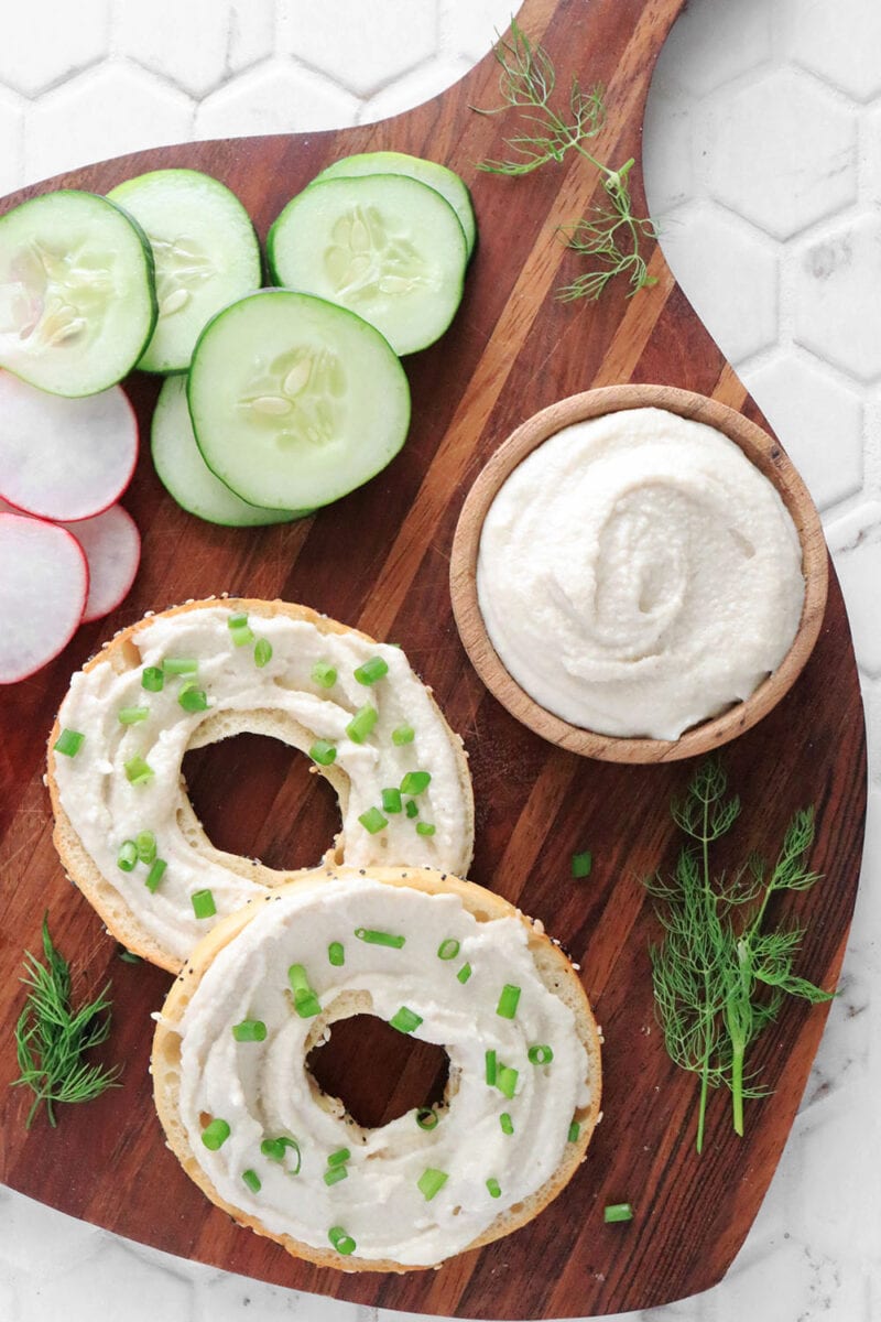Vegan cream cheese spread on two bagels on a cutting board
