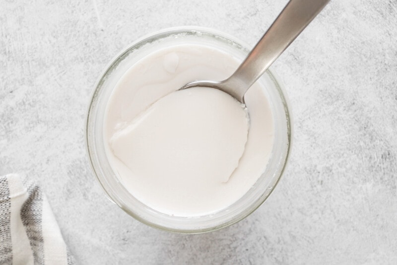 Thickened vegan greek yogurt ingrediants in a glass container with a spoon.