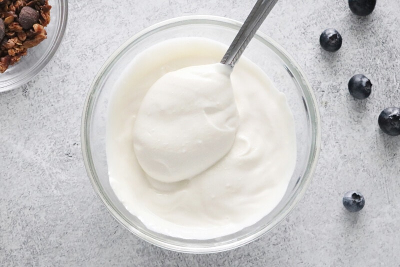 A spoon dipped into a small bowl of vegan Greek Yogurt.