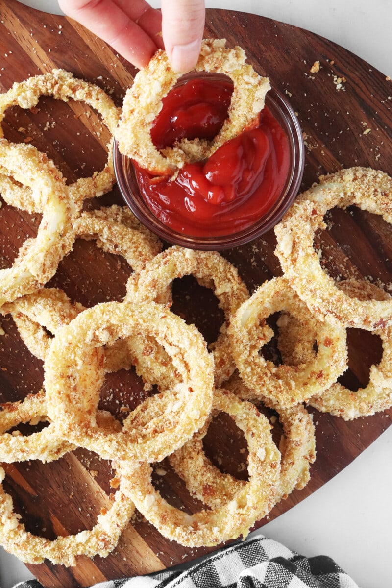 Vegan crispy baked onion rings on a serving board served with a side of ketchup.