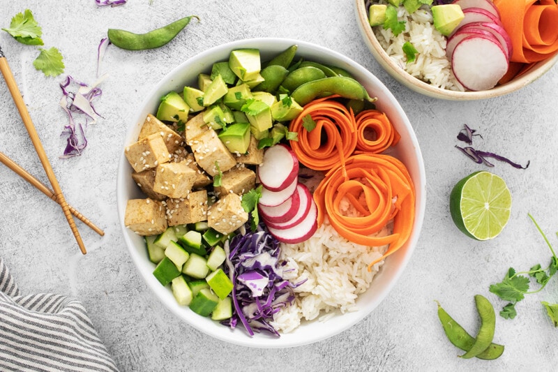 Vegan tofu poke bowl with marinated tofu, avocado, thinly sliced carrots, purple cabbage, cucumber, edamame, and radishes.