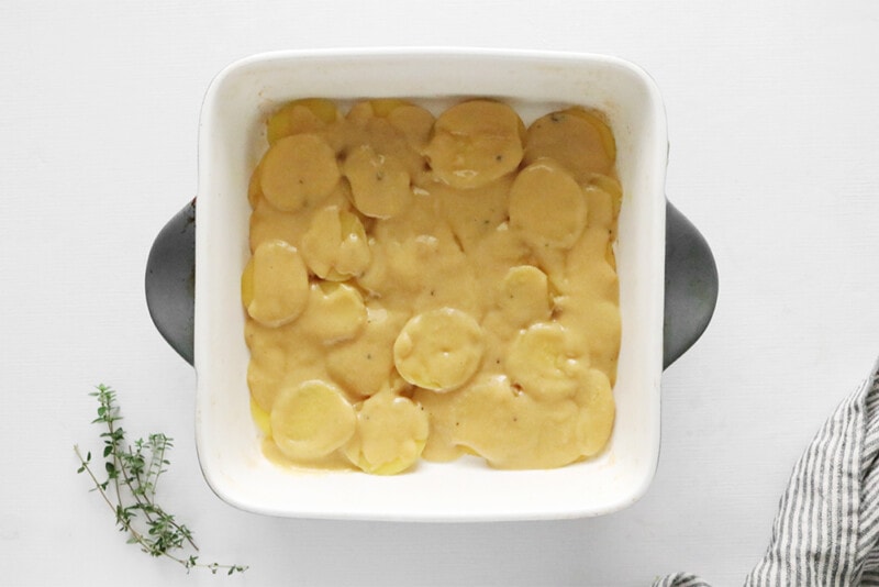 creamy sauce poured over scalloped potatoes in a casserole dish