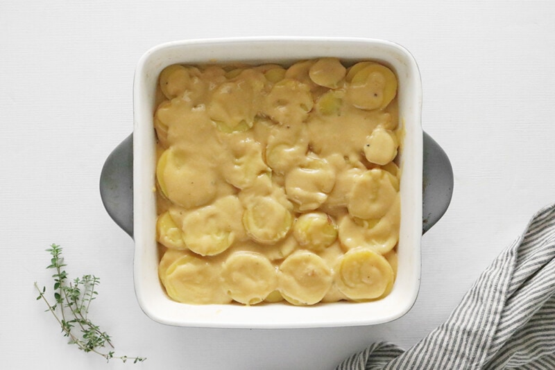 layers cheese sauce and scalloped potatoes in a casserole dish