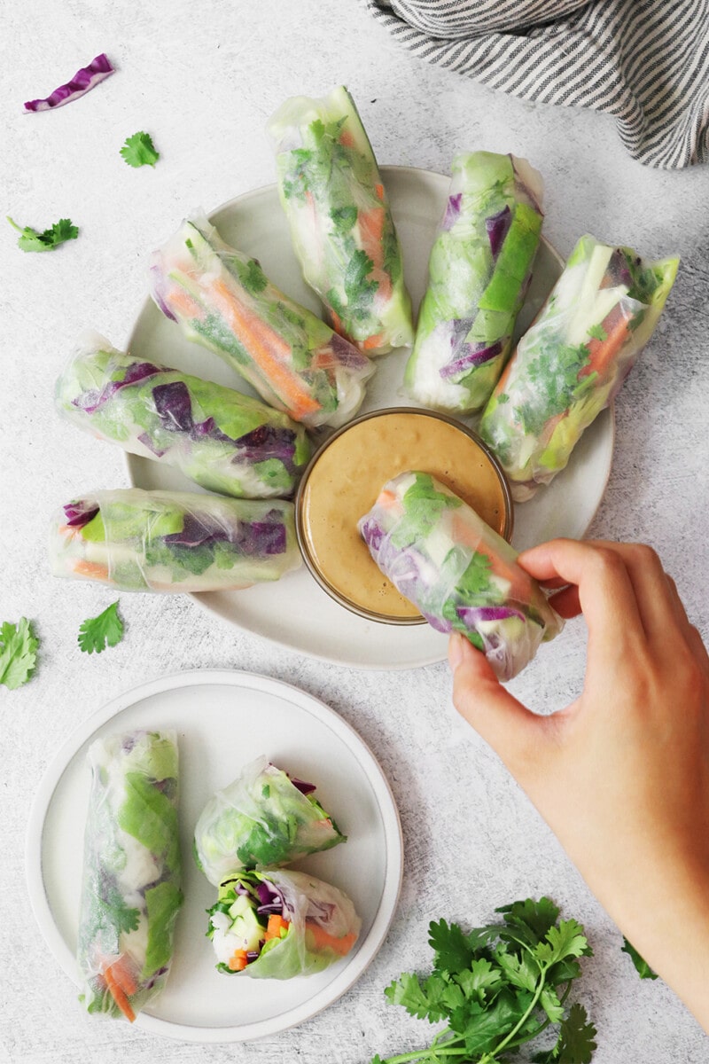 Vegan spring rolls, filled with lettuce, cabbage, and sliced vegetables, served with a side of peanut sauce.