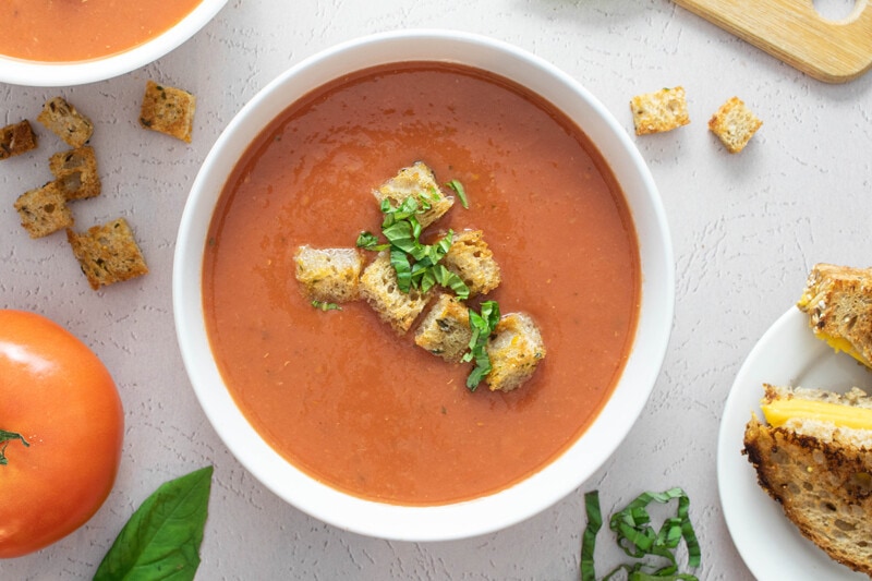 Vegan tomato soup in a bowl, topped with croutons and fresh basil.