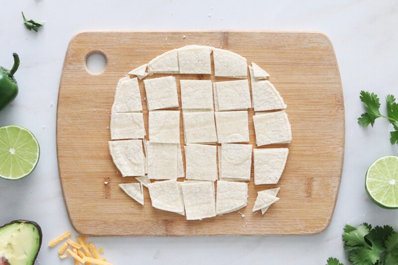 A corn tortilla on a cutting board cut into squares.