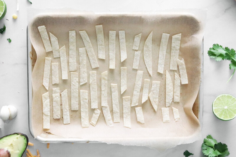 Tortilla strips arranged on a baking sheet lined with parchment paper.