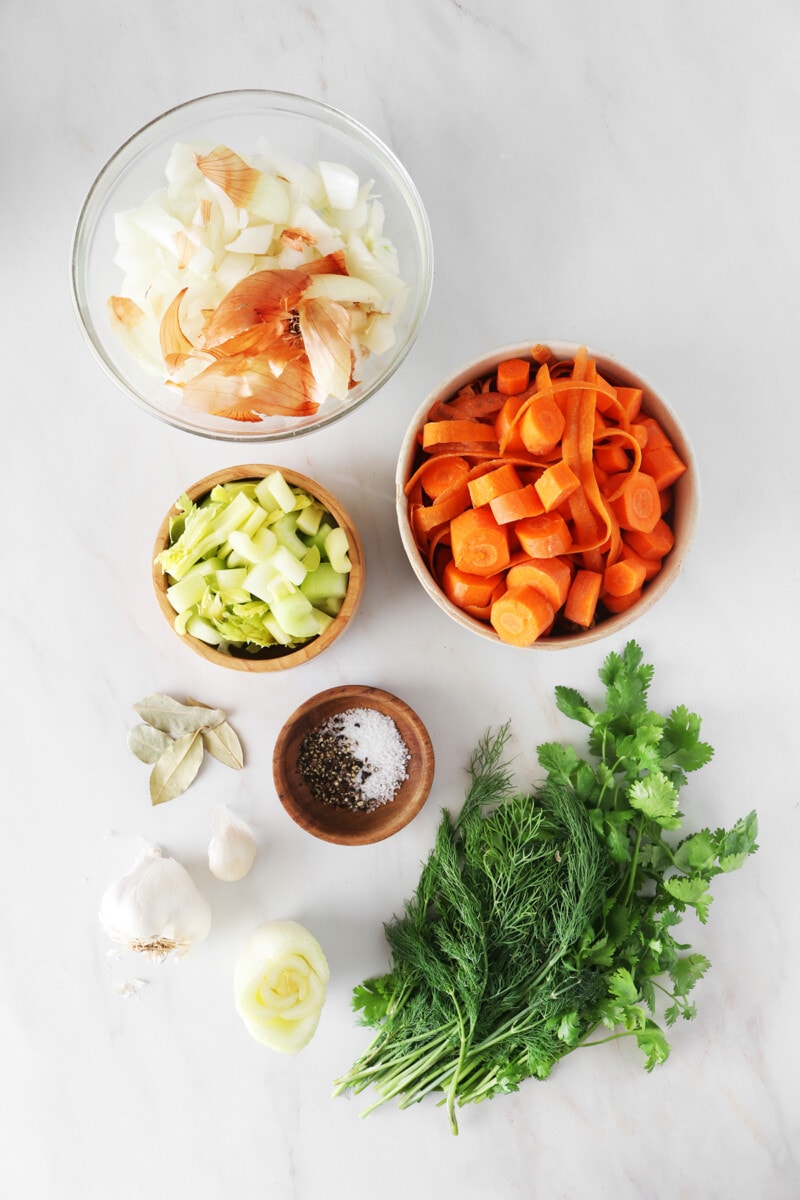 Ingredients for vegan vegetable broth: Onion scraps, carrots, celery, garlic, leek, bay leaves, salt, pepper, and fresh herbs.