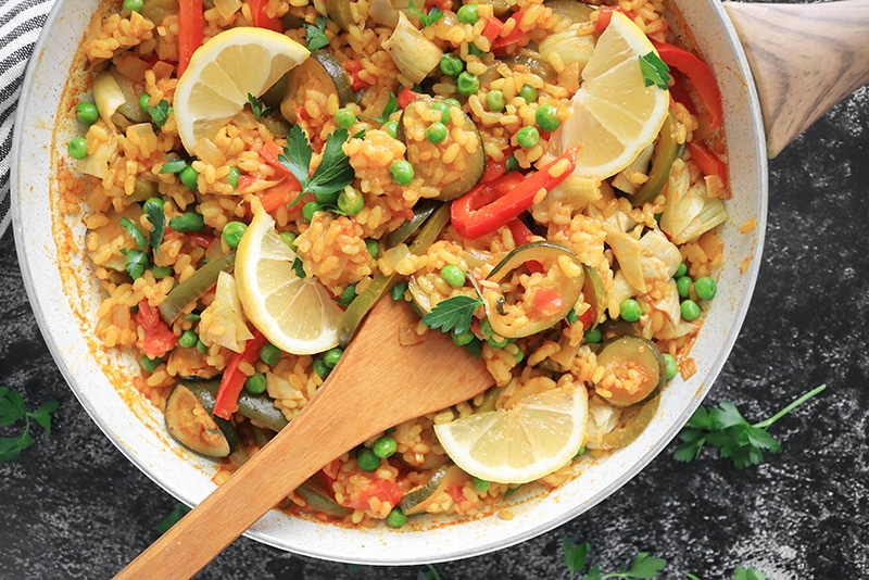 Vegetarian Paella being served with a wooden spoon in a skillet
