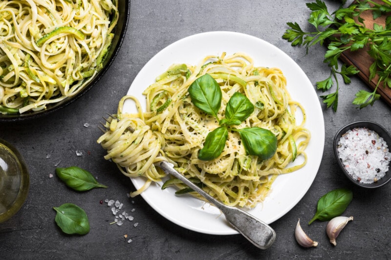 Vegetarian pasta and basil leaves on a white plate with dark background