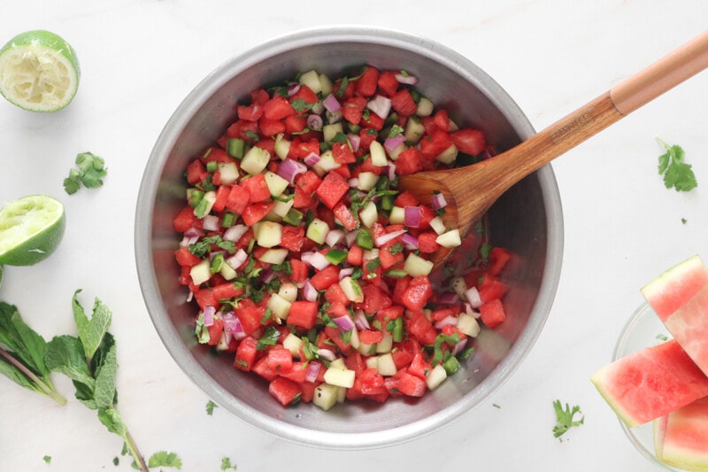 Watermelon Salsa ingredients in a stainless steel bowl with a wooden spoon.