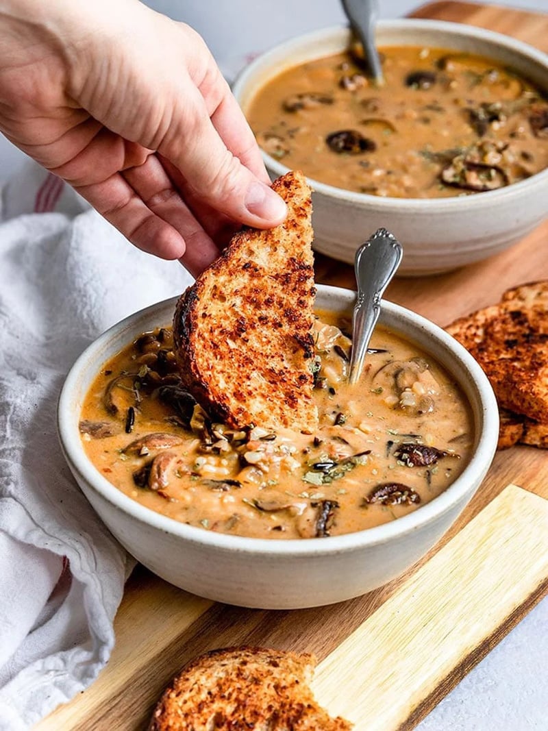 Dipping toasted whole grain bread into a creamy bowl of wild rice mushroom soup.