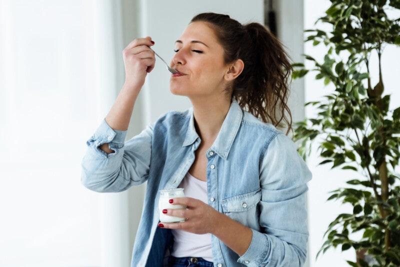 A beautiful young woman eating yogurt at home.