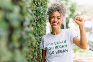 Happy mature woman advocating for veganism while wearing a shirt with the words "GO VEGAN" written on it.