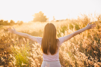 woman raising her hands in meadow grass field with warm sunshine