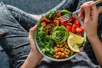 Woman with ripped jeans eating healthy vegan food from a bowl.