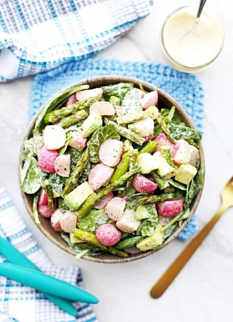Roasted asparagus with radishes tossed in a creamy garlic cashew dressing in a bowl.